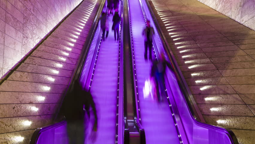 Timelapse of blurred shoppers riding an escalator at a shopping mall
