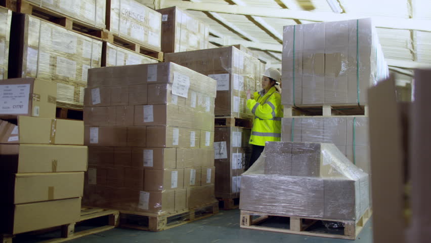 2 industrial workers are walking between rows of merchandise in a factory or warehouse and checking that the goods are adequately packed and stored