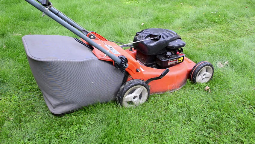 man gardener worker in shorts and blue rubber boots walk push grass lawn cutter mower on meadow