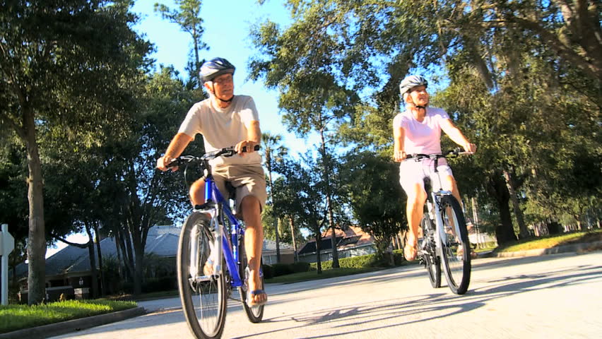 Mature couple wearing safety helmets keeping fit riding their bicycles outdoors on suburban roads