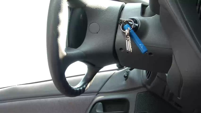 Man breaks into his own car and unlocks door with wire hanger and keys in ignition, (in shot entire time), natural light.