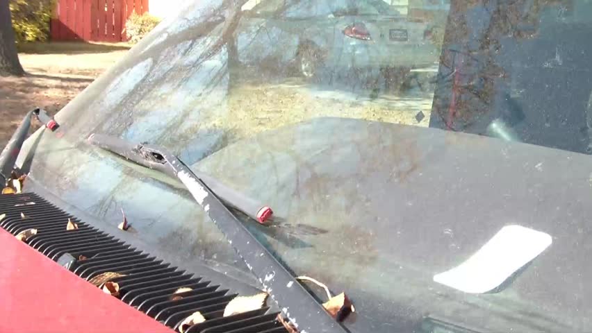 Bright orange police tow notice is placed on windshield, under wiper blade, in daylight.