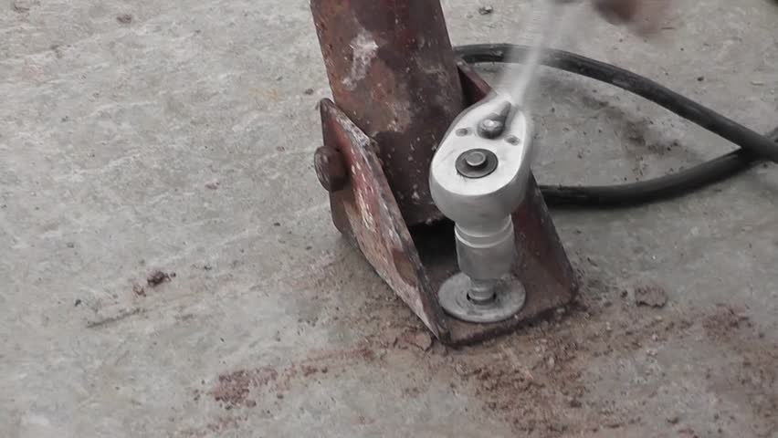Man tightening a bolt or screw using a socket and ratchet spanner to hold a steel fixture in place on concrete at a construction site