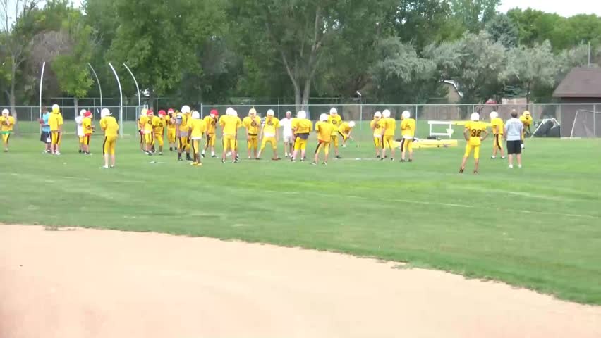 Youth football team practices by scrimmaging each other with colored helmets, in natural lighting.