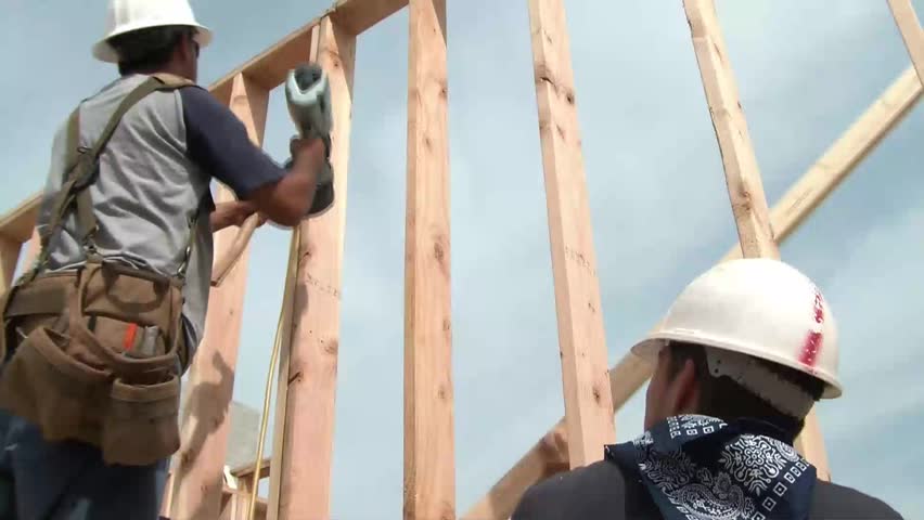 Construction worker uses a air powered nail gun and swings a hammer at a stud on new wood framing.