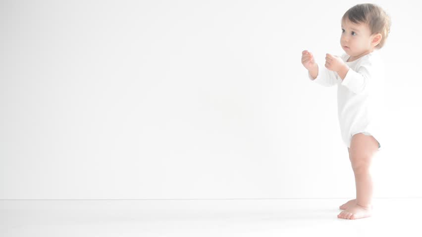 Happy little baby making first steps on white floor