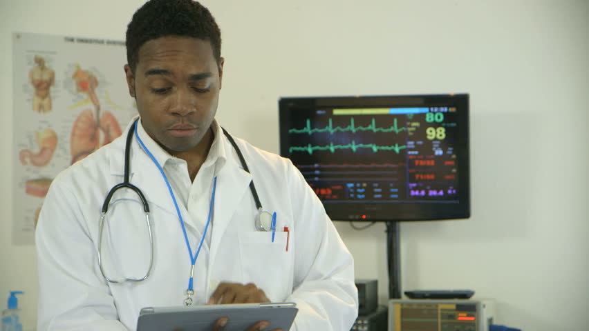 A young African American intern or physician goes looks up from what he is studying on an electronic tablet and smiles confidently.