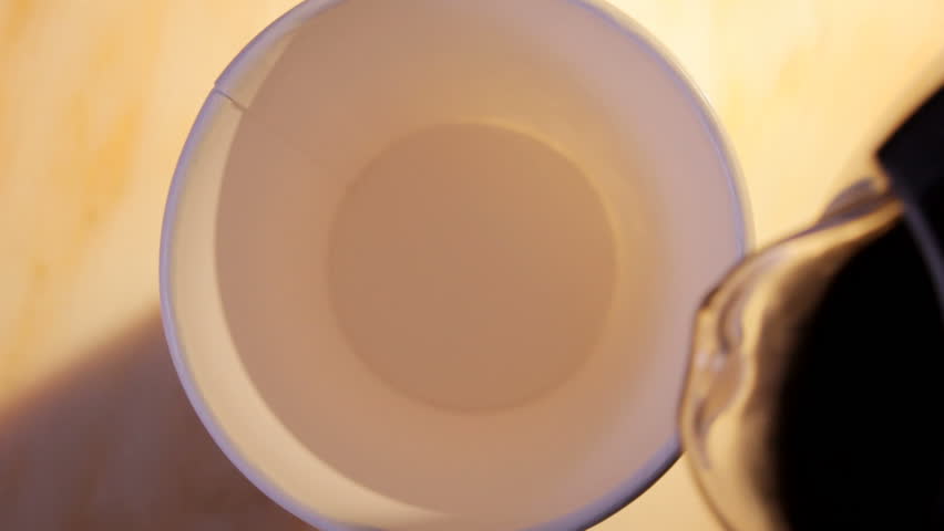 close up HD video of coffee and milk pouring into paper cup, hand takes cup away from right side.