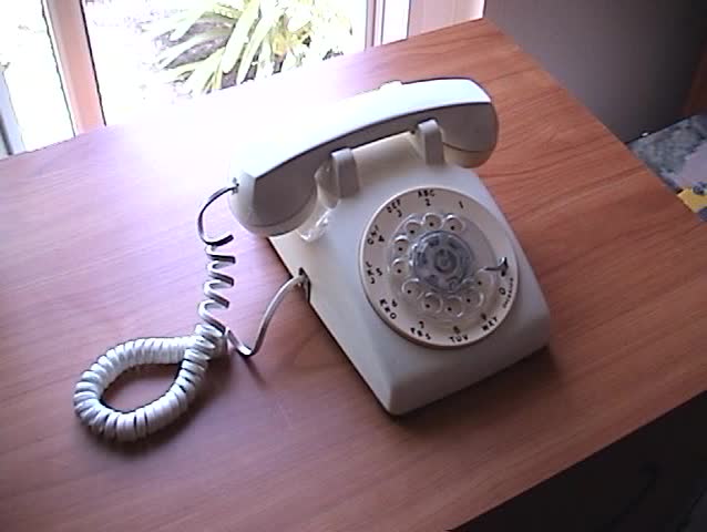 a person picks up the receiver and dials a fictitious phone number on an old rotary telephone