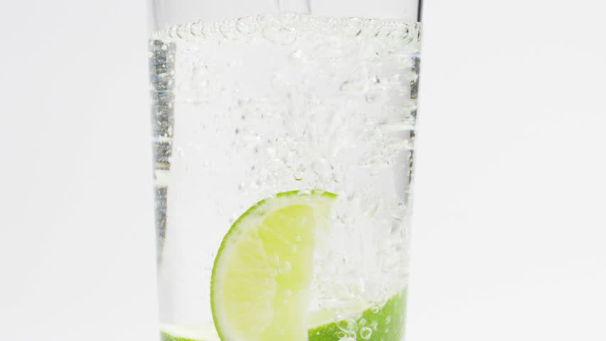 Slow motion (300 fps) shot of a glass filled with ice cubes, lime, and sparkling water, creating a refreshing drink.