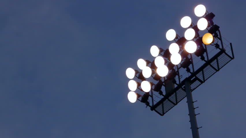 Rack focus of stadium lights in front of a dark blue sky.