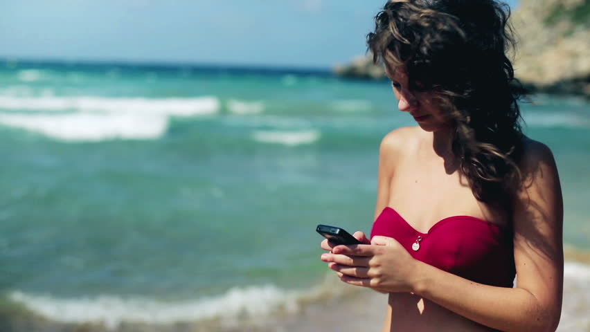 Young woman standing on the beach and texting message using cellphone
