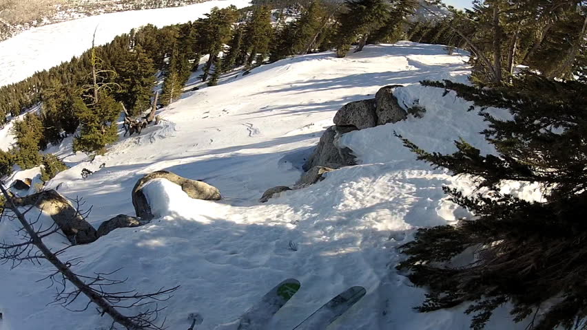 A skier carves back and forth as he rides down a mountain covered in fresh powder during the day. It is shot with a camera mounted to the athletes head and provides a POV, point of view, perspective.