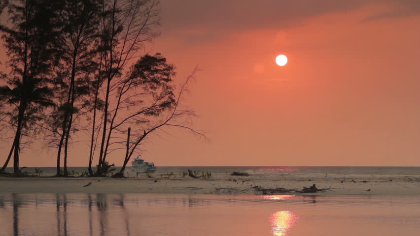 Sunset over the sea and sandbar and boat crossing the gulf on Koh Kood Island, Thailand