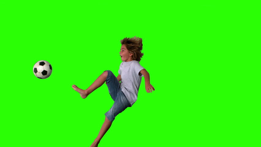 Boy jumping and kicking football on green screen in slow motion