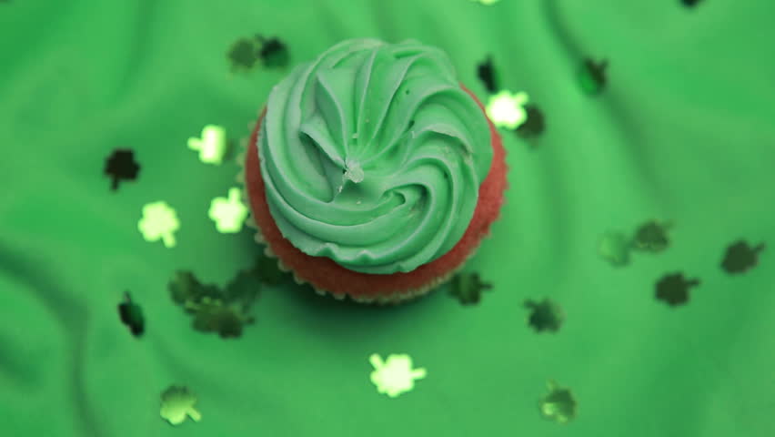 St patricks day cupcake revolving with shamrock confetti falling on green surface