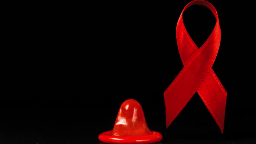 Condom falling over in front of a red ribbon on black background in slow motion