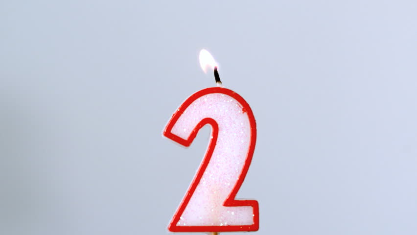 Two birthday candle flickering and extinguishing on blue background in slow motion