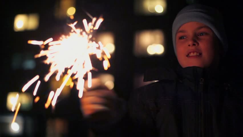 Cheerful boy holds Bengal fire in hand near house at winter night