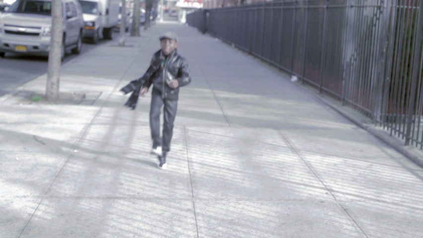 African American Black kid with hat skipping outside in the street in the day