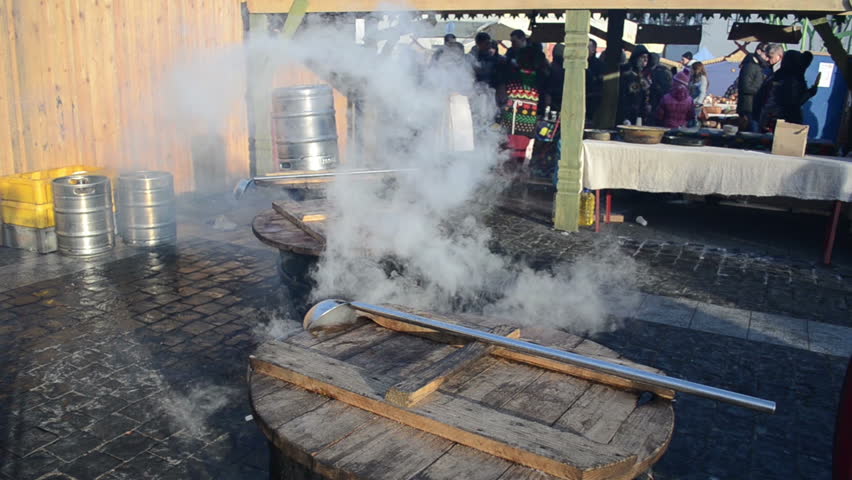 VILNIUS, LITHUANIA - MARCH 02: People buy hot drink wine boil from huge pots in spring outside street market fair on March 02, 2012 in Vilnius. Fire burn and smoke vapour rise.