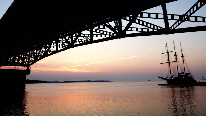 Sunrise time-lapse under bridge with sailing ship