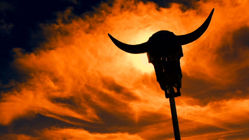 Time Lapse, Cow skull, propped on stick, creates eerie, spooky, creepy visual as fiery sky seeps through cracks in skeleton, eye sockets. 1080p