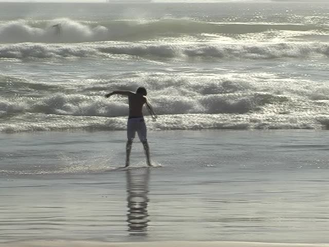 Young boy sliding on a sand-board floating on the water and falling into the waves Ã¢â¬â Silhouette, with ships in background - Editorial use only