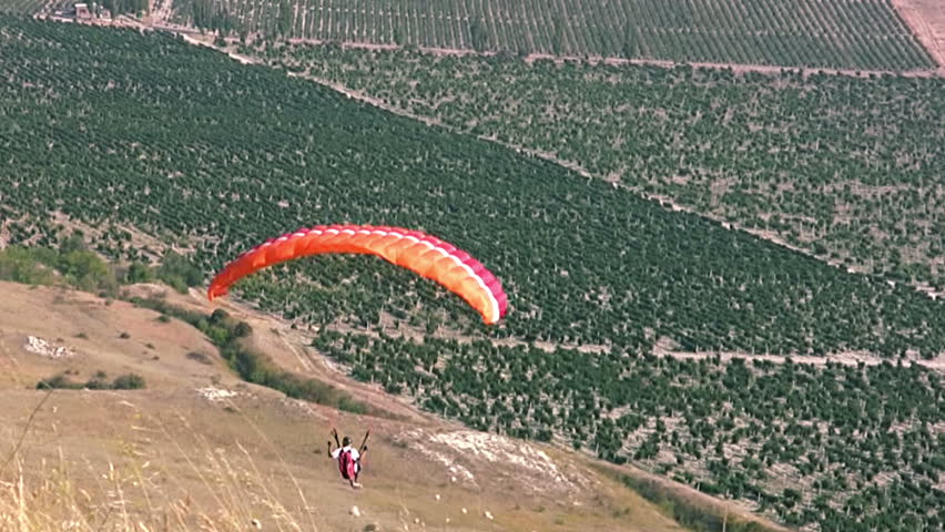 Summer. Clear weather. Paraglider drops sharply over field and then rises over the shoreline
