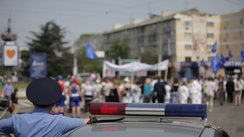 Police car standing next to people walking at demonstration.