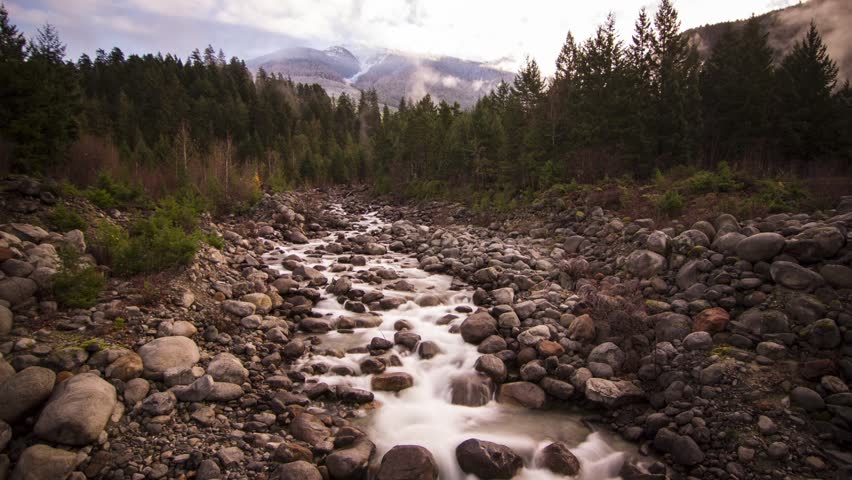 Misty Clouds on a Snowy Mountain Top and River Running by Lillooet Lake in BC, Canada. Photo Sequence shot in RAW and Post-Production in After Effects