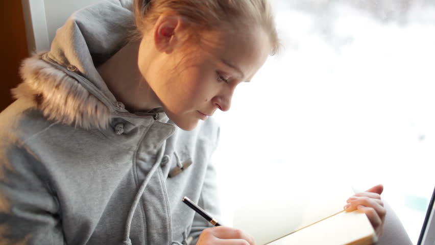 Young beautiful girl writing in her journal and daydreaming.