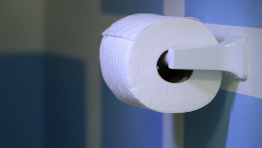 Close up on hand taking sheets of paper from a toilet roll in a rest room.