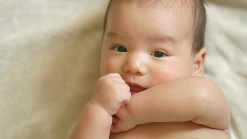 Close up of a happy three month old, Asian-American baby boy wriggling around and laying on a soft blanket.