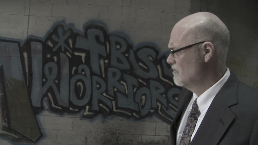 Businessman walks past graffiti in broken down building, then out into bright, white light which fills the screen.