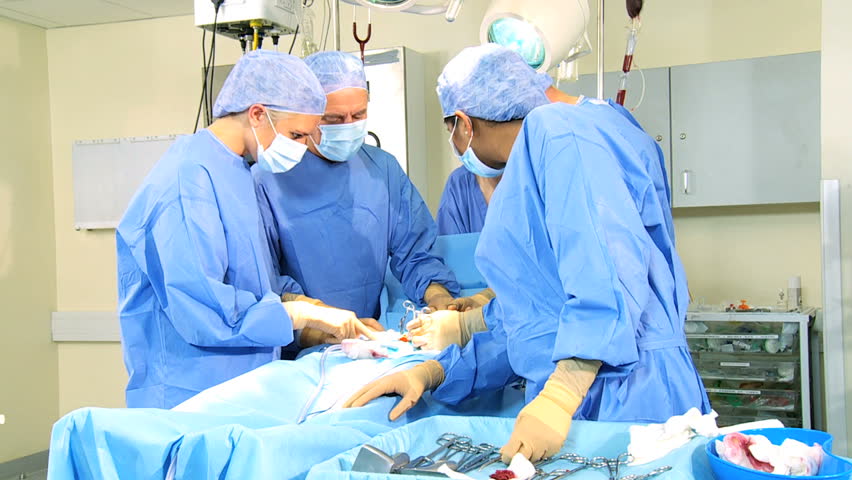 Senior doctor performing operation using surgical equipment helped by surgical team anesthetist