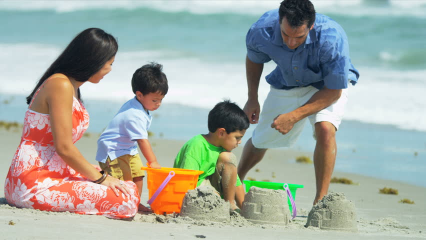 Happy Hispanic family building sand castles on beach shot on RED EPIC