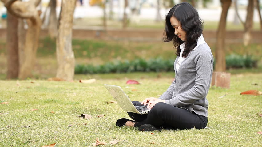 female is typing on the laptop in the park