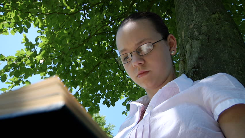 A teenage girl reads a book under a tree