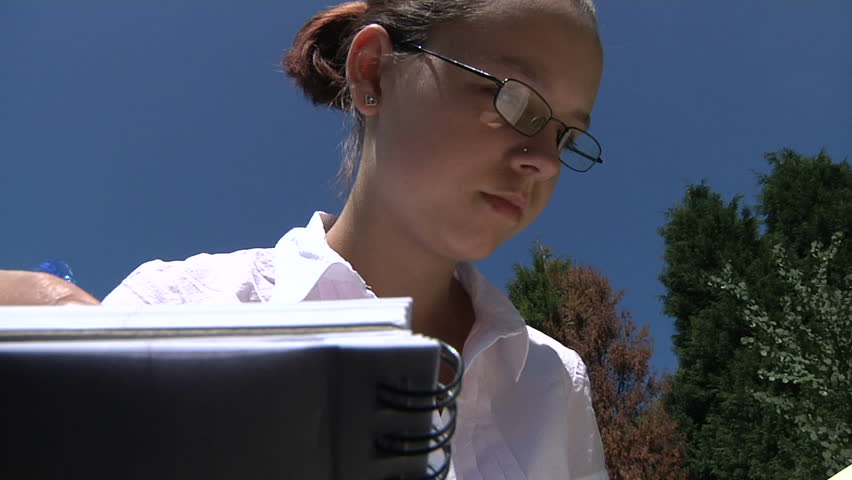 A student studying outdoors with textbook and folders