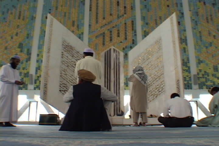 PESHAWAR AND ISLAMABAD, PAKISTAN - NOVEMBER 01, 2001: Men standing and praying in front of large replica of the Koran inside Faisal Mosque.