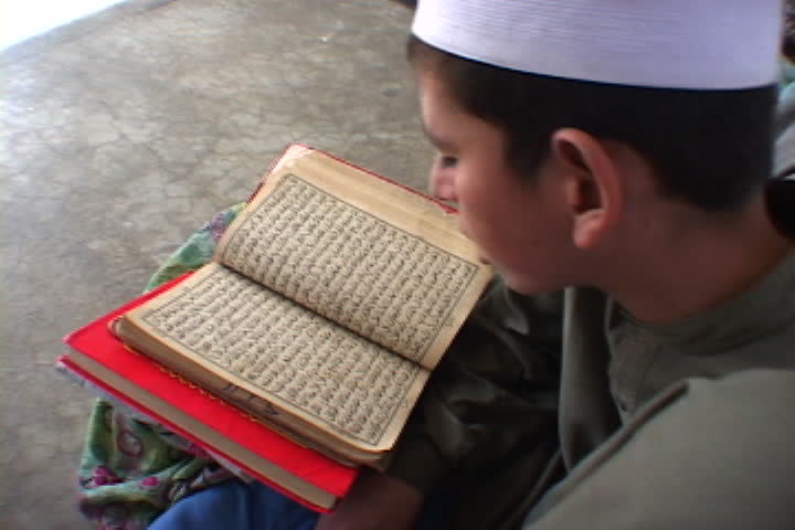 PESHAWAR, PAKISTAN - NOVEMBER 01, 2001: Over the shoulder shot of boy in Muslim dress rocking back and forth as he reads his open Koran.