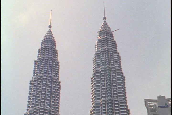 KUALA LUMPUR - OCTOBER 22, 1999: Exteriors of Petronas Towers and plaza; MS tops of towers, tilt down length of building to plaza and kids playing in shallow pool.