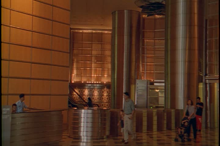 KUALA LUMPUR - OCTOBER 22, 1999: Petronas Towers lobby interiors; CU of brass pillar, camera pans left to show WS of main lobby and information desk, pedestrians walking through lobby.