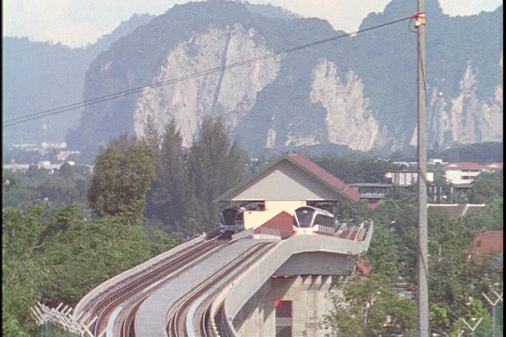 KUALA LUMPUR - CIRCA OCTOBER 1999: Lake Garden tram station with tall green mountains in background. Train leaves the station and heads toward camera.
