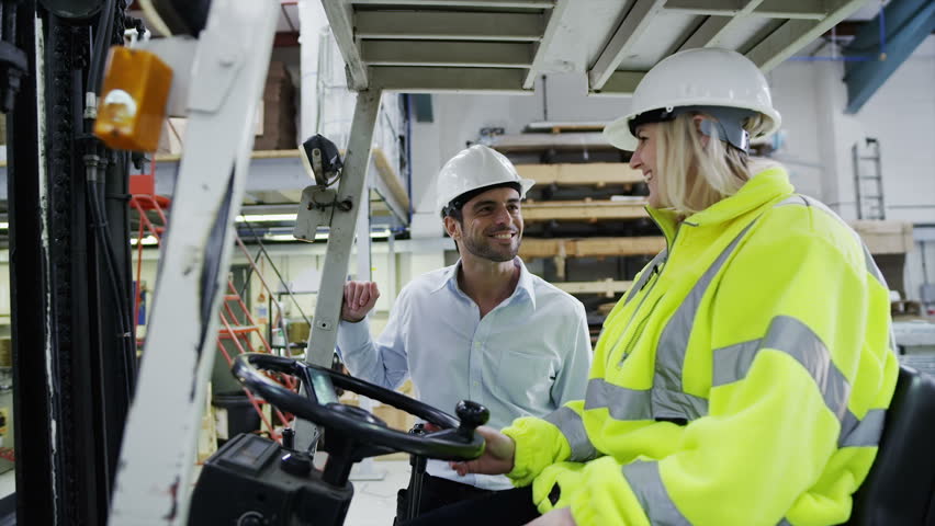 A male forklift truck driver arrives on shift in a factory or warehouse to take over from his female co-worker. 