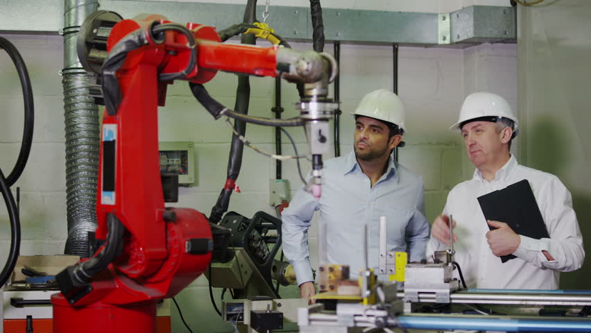 A mature male factory manager is with a young male client or colleague and is explaining how some of the plant machinery works. 