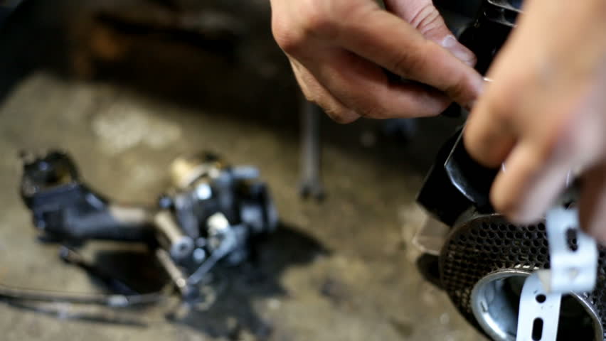 Young man cleaning a dirty engine of a mini motor. A lot of oil. Working in workshop on the floor. Unscrewing parts of the motor.