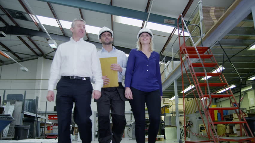 Happy and friendly team of workers in a warehouse or factory come together as they walk around the factory floor. They may be the owners of the business or part of the company team.