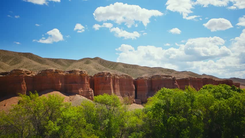 Timelapse over the Charyn (Timerlik) Canyon. Fluffy clouds above red rock mountain peak. Natural landscape erosion and grand canyons with stunning rock formations.